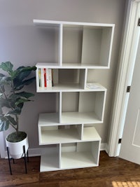 a white bookcase in a room with a plant